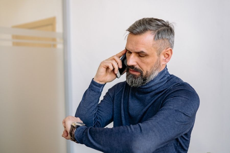 Man on the phone checking his watch while waiting for a restoration company to respond to an emergency